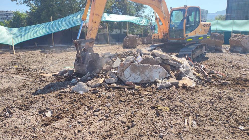 Excavadora retirando restos de hormigón en un terreno con cierre de obra