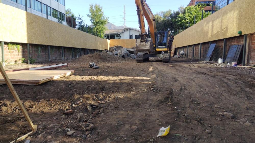 Terreno despejado tras la demolición, con excavadora entre cierros de obra